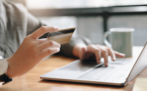 Close up of a person's hands holding a credit card and using a laptop