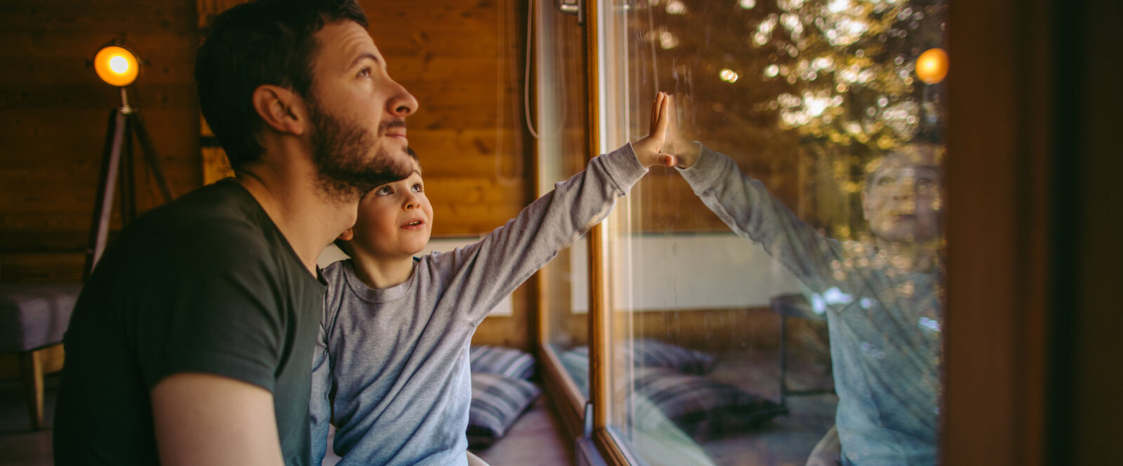 Man holding a young boy looking out a large window